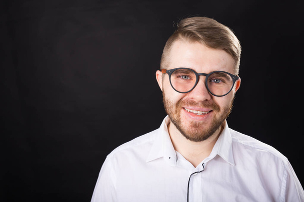 Portrait of young smiling bearded man and in glasses over the black background with copy space - Photo, image