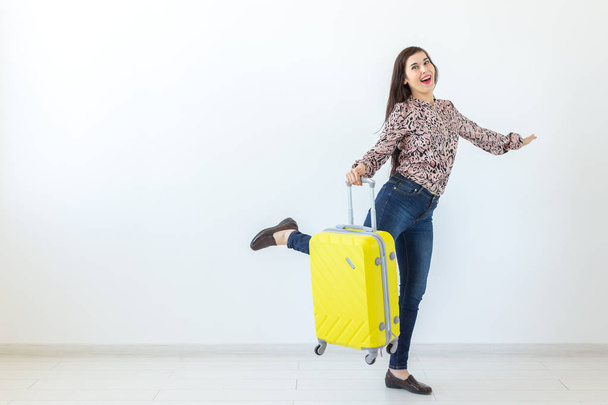 Slim positive young brunette woman posing with a yellow suitcase on a white background with copy space. Concept of tourism and holidays - Foto, Imagem