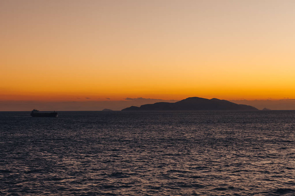 Ship sailing at sunset with island silhouette background and orange sky - Фото, изображение
