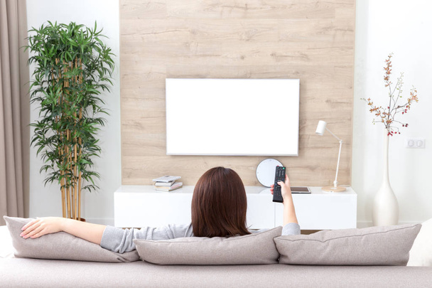 Молодая женщина смотрит телевизор в комнате. белый пустой экран для дизайна
 - Фото, изображение