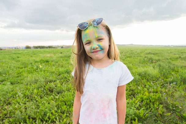 Діти, фестиваль холі та канікул концепція - щаслива дівчинка в сонцезахисних окулярах, покритих кольоровим порошком, посміхається на фоні природи
 - Фото, зображення