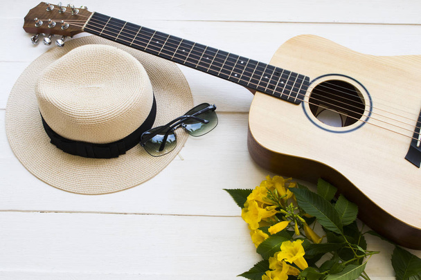 гитара, солнцезащитные очки и шляпа образа жизни женщина расслабиться летом с желтыми цветами расположение плоский стиль лежа на фоне белого дерева
 - Фото, изображение