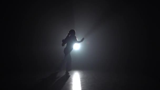 Profesionální tanečník trénuje capoiru v temnotě proti reflektoru ve studiu. Zpomaleně. - Záběry, video