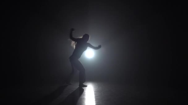 Dama hábil practicando capoeira en la oscuridad contra el proyector en el estudio. Movimiento lento
. - Metraje, vídeo