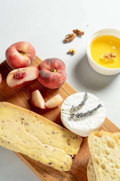 Top view different types of cheeses on wooden cutting board. Cheese with fig peach, honey, ciabatta and nuts, glass of red wine. Stylish food flat lay on grey background. Copy space. Soft focus - Foto, Bild