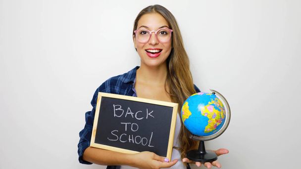 Beautiful young female student holding globe and blackboard with written back to school. - Photo, Image