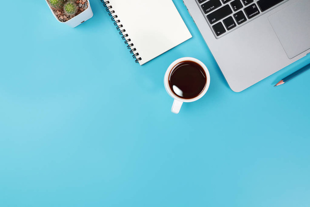 Business Office tabel met werkruimte, laptop computer, koffie kopje, notebook, potlood, plant en mobiele telefoon op blauwe pastel achtergrond - Foto, afbeelding