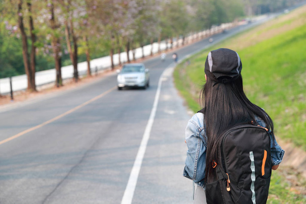 Jovem asiático viajante com mochila esperando carro na estrada enquanto viaja durante as férias
 - Foto, Imagem