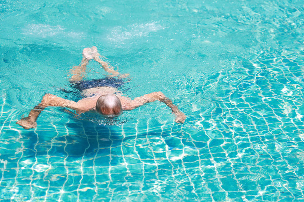 happy elderly caucasian swimming in pool during retirement holiday with relaxation and smiling - Photo, Image