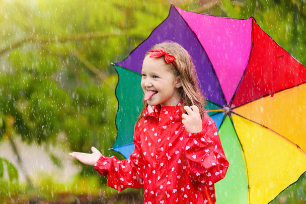 Kid with umbrella playing in summer rain. - 写真・画像