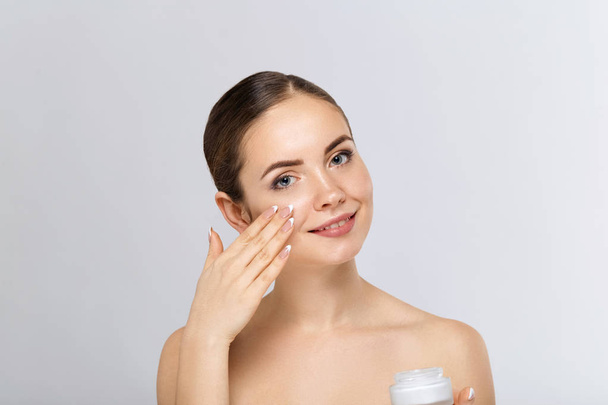 Beauty Woman Face Skin Care. Portrait Of Attractive Young Female Applying Cream  And Holding Bottle. Closeup Of Smiling Girl With Natural Makeup And Fresh Skin. Beauty Cosmetics. - Foto, immagini
