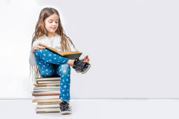 A pretty girl is sitting on a stack of books and reading a book  - Photo, image
