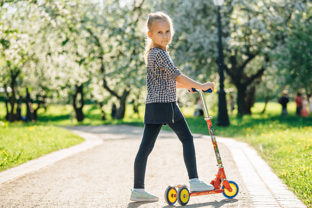 Active little toddler girl riding scooter on road in park outdoors. Seasonal child activity sport. Healthy childhood lifestyle - Fotoğraf, Görsel