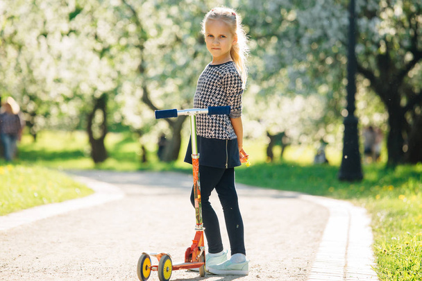 Active little toddler girl riding scooter on road in park outdoors. Seasonal child activity sport. Healthy childhood lifestyle - Foto, imagen
