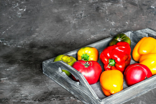 Imperfect natural peppers and tomatoes on an old wooden tray on a dark background. Copy Space. - Fotó, kép