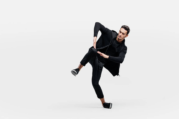 Handsome young man wearing a black sweatshirt and black pants is dancing breakdance - Фото, изображение