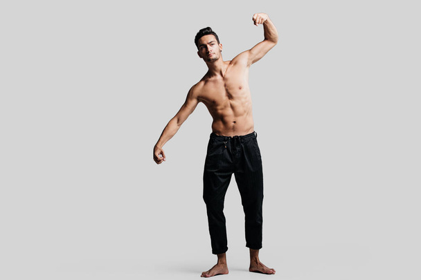 Dark-haired handsome young dancer with bare torso wearing a black pants makes dancing movements on a white background - Foto, Bild