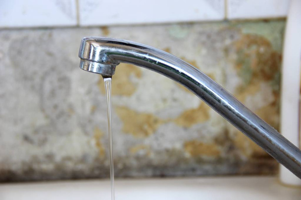 un flusso sottile di acqua scorre dal rubinetto, rubinetto da cucina color argento su sfondo vecchio muro
 - Foto, immagini