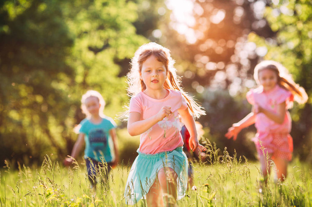 Large group of kids, friends boys and girls running in the park on sunny summer day in casual clothes . - 写真・画像