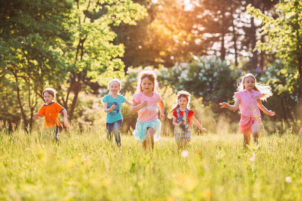 Large group of kids, friends boys and girls running in the park on sunny summer day in casual clothes . - Fotó, kép