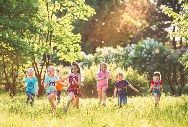 Large group of kids, friends boys and girls running in the park on sunny summer day in casual clothes . - Fotó, kép