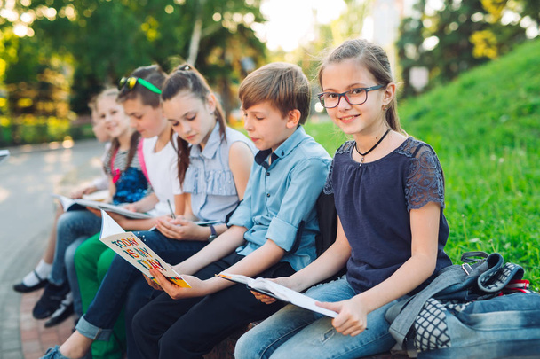 Szczęśliwego Portretu kolegów ze szkoły. Koledzy ze szkoły siedzą z książkami w drewnianej ławce w parku miejskim i uczą się w słoneczny dzień. - Zdjęcie, obraz