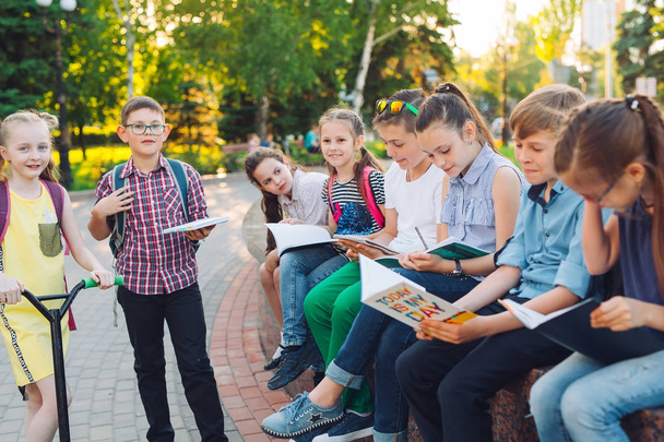 Щасливий портрет школярів. Школярі сидять з книгами на дерев'яній лавці в міському парку і навчаються в сонячний день
. - Фото, зображення