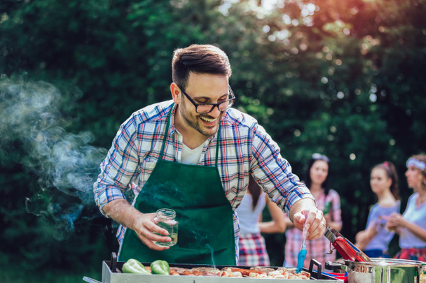 Красивый мужчина готовит барбекю на открытом воздухе для друзей
 - Фото, изображение