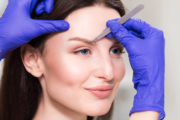 Cosmetologist plucks client eyebrows by tweezers - Photo, image