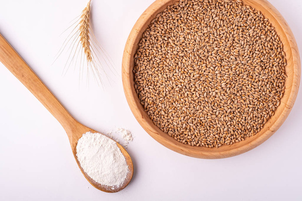 小麦の種子は、スプーンのへらで小麦粉と小麦の耳で近くの木製のボウルの穀物、 トップビュー、 フラットレイ、 白い背景に隔離された、コピースペース - 写真・画像
