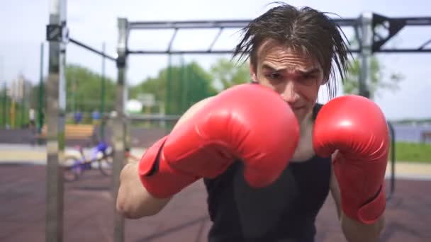 Zwolnionym. Młody muskularny bokser w czerwone rękawiczki robi ciosy w aparacie, stały strzał - Materiał filmowy, wideo