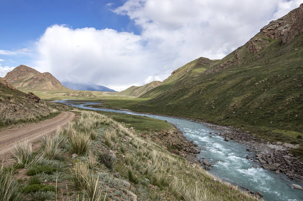Θέα του ποταμού που ρέει ανάμεσα στους πράσινους λόφους με γρασίδι και πέτρες στο προσκήνιο Κιργιστάν. - Φωτογραφία, εικόνα