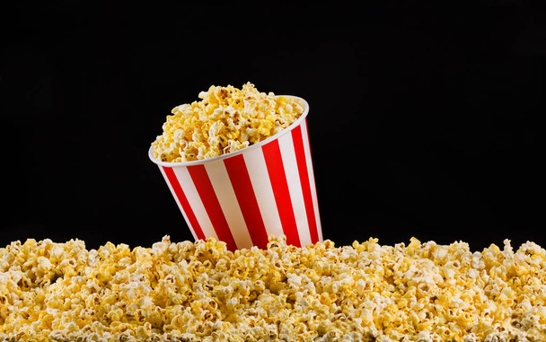 Paper striped bucket installed on scattered popcorn isolated on black background - Photo, image
