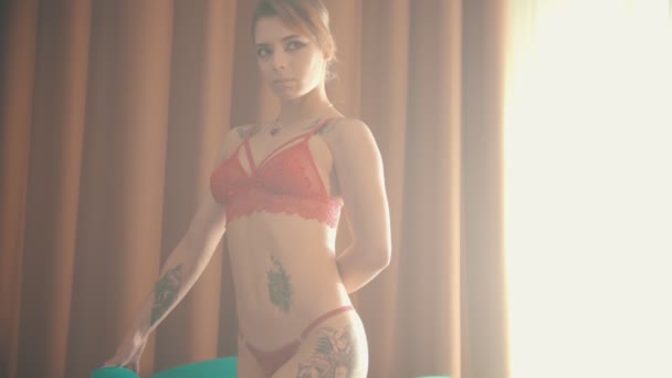 Молодая женщина со множеством татуировок в сексуально-красном белье, стоящая на стуле
 - Кадры, видео