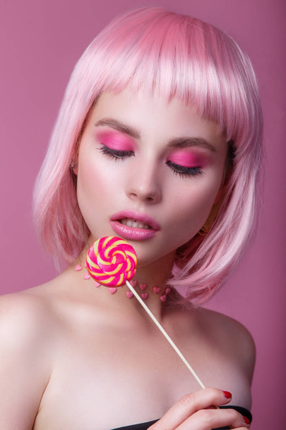 Mulher glamour beleza com cabelo rosa e bela maquiagem segurando doce rosa colorida pirulito doce
 - Foto, Imagem