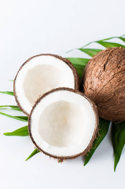Coco maduro medio cortado con hojas verdes sobre un fondo blanco. Concepto aislado
.  - Foto, Imagen