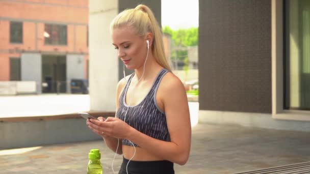 Young, attractive and sporty blond girl in sportswear listening to the music and relaxing outdoor. Healthcare, sport, fitness and lifestyle. - Filmagem, Vídeo
