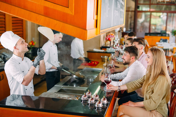 O chef prepara comida na frente dos visitantes no restaurante
 - Foto, Imagem