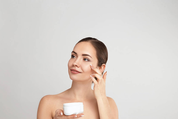 Facial Care. Female Applying Cream and Smiling. Portrait Of  Young Woman With Cosmetic Cream On Skin. Closeup Of Beautiful Girl With Beauty Product On Soft Skin, Natural Makeup Touching Face. - Valokuva, kuva