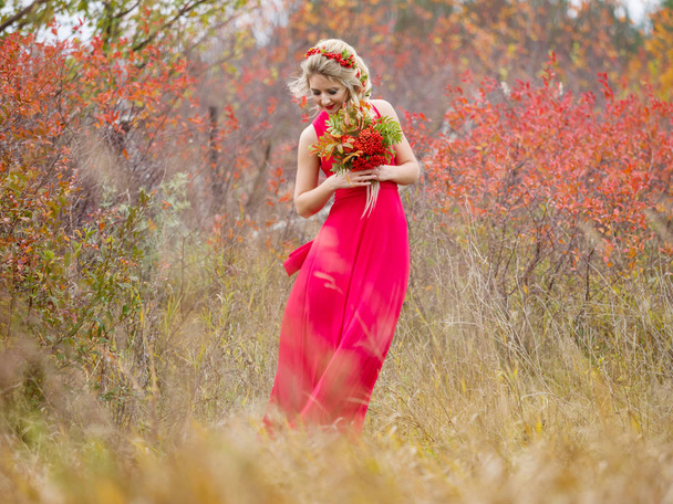Όμορφο κορίτσι σε ένα κόκκινο μακρύ φόρεμα με ένα κούρεμα και με ένα φθινοπωρινό Μπουκέτο ανθοδέσμη την ημέρα του φθινοπώρου σε ένα πεδίο στη φύση - Φωτογραφία, εικόνα