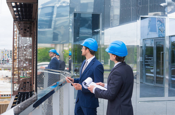 Real estate developers in helmets. New office construction. Confident business men and architect talking in front of modern office building. - Photo, Image