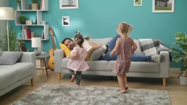 Twee kleine dochters wekken vader die slaapt op een bank in de woonkamer - Video