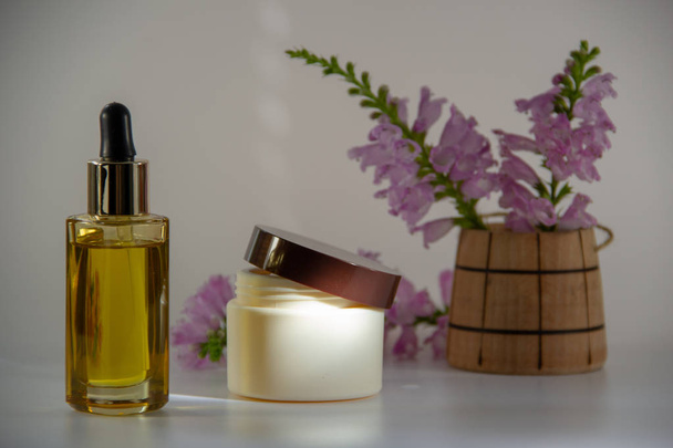 Gold natural face oil in a glass bottle with a dropper, packaging for face cream, a fragrant bouquet of flowers in a wooden barrel on a white background. - Foto, Imagen