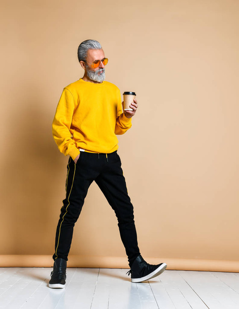 Vertical shot of a joyful senior holding a white coffee cup and looking at the camera - Фото, изображение