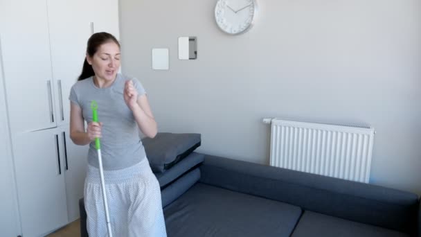 Mutlu kadın paspas kullanarak zemin yıkıyor, bir şarkı söylüyor ve modern dairesinde dans ediyor.. - Video, Çekim