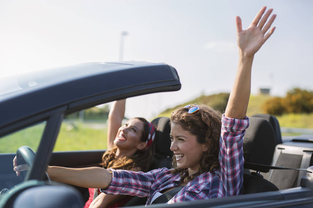 Two young beautiful girls driving in a convertible - Foto, Imagen