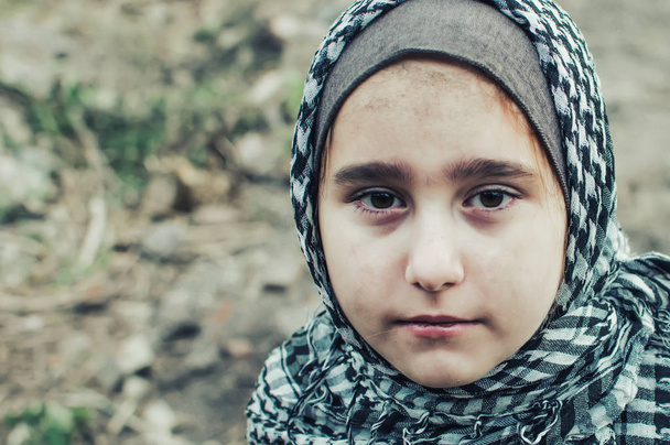 ein Flüchtlingskind im Krieg, ein muslimisches Mädchen mit schmutzigem Gesicht auf den Trümmern, das Konzept von Frieden und Krieg, das Kind weint und wartet auf Hilfe. - Foto, Bild