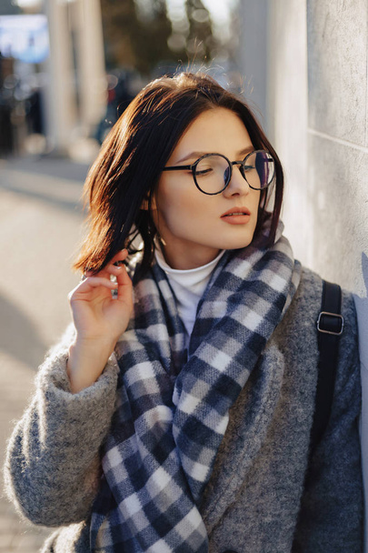 Attractive young girl wearing glasses in a coat walking on a sunny day - Φωτογραφία, εικόνα