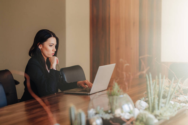 Młoda atrakcyjna dziewczyna emocjonalna w biznesie w stylu ubrania siedzi przy biurku na laptopie i telefon w biurze lub audytorium - Zdjęcie, obraz