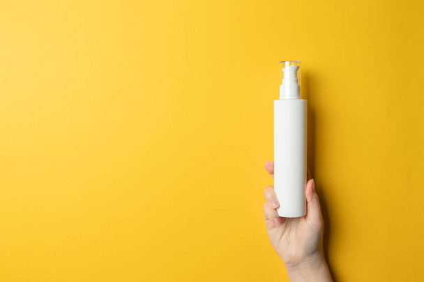 La mano femenina sostiene un frasco de cosméticos blancos de plástico con líquido o loción para el cuidado de la piel
 - Foto, Imagen